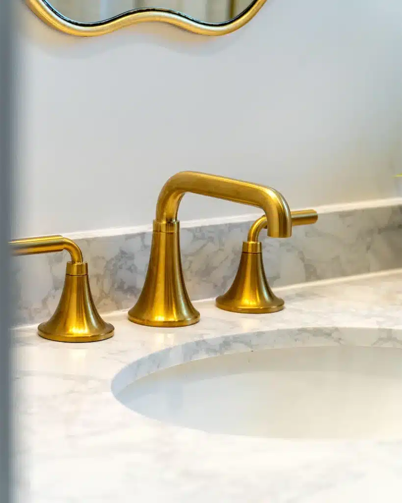 A gold faucet sits on top of a white, brushed marble counter top.