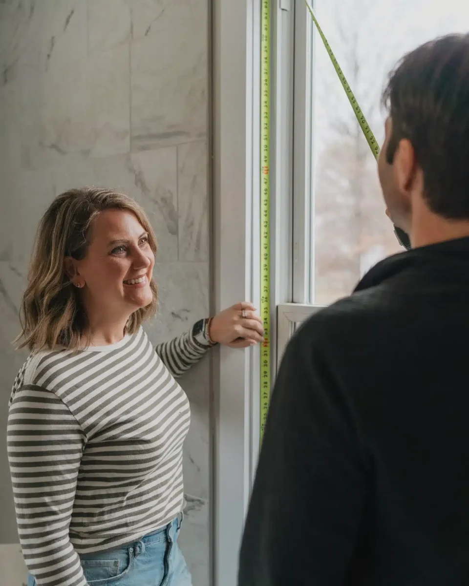 Paul and Rebecca Presson measure the height of a window in a tiled bathroom.